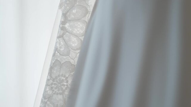 Close-up detail of delicate floral lace fabric on a white wedding dress with a soft blurred background.