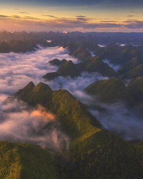 Aerial view of the lush green mountains of Bac Son valley rising above a sea of clouds during a golden sunrise in Bac Son, Lang Son, Vietnam.