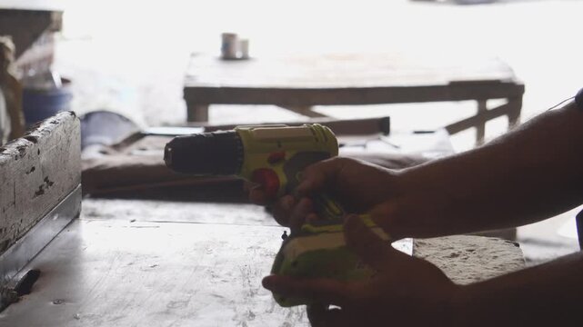 Close-up of a carpenter using a cordless electric drill to screw into a wooden plank in a woodworking workshop, handyman at work.