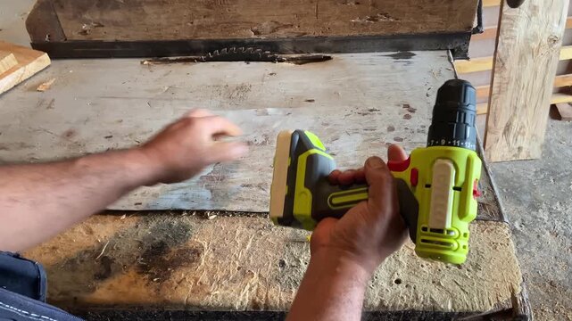 Close-up of a carpenter using a cordless electric drill to screw into a wooden plank in a woodworking workshop, handyman at work.