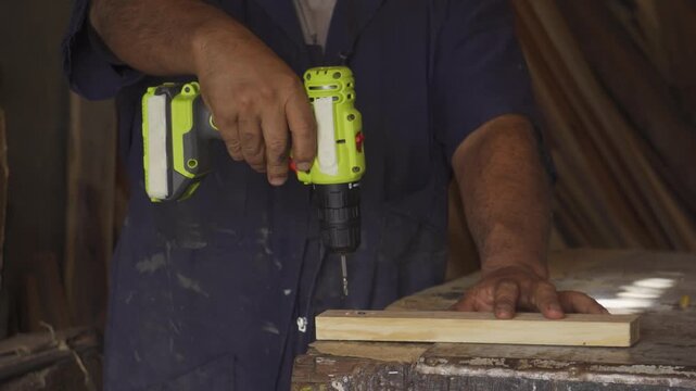 Close-up of a carpenter using a cordless electric drill to screw into a wooden plank in a woodworking workshop, handyman at work.