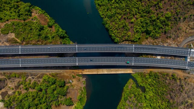 Aerial view of the Hindu Hrudaysamrat Balasaheb Thackeray Maharashtra Samruddhi Mahamarg bridge crossing a river with lush green vegetation and rugged landscape in Kasara, Maharashtra, India.