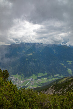 Aerial view of Konigssee lake nestled in the lush green valley surrounded by dramatic alpine mountains under a cloudy sky in Schonau am Konigssee, Bavaria, Germany.