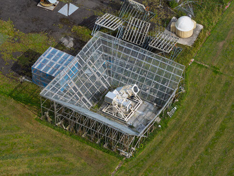 Aerial view of a radio telescope structure with a large metal mesh reflector and complex mechanical equipment set in a grassy field in the United Kingdom.