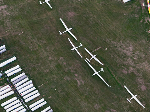 Aerial view of several white gliders parked on a grassy airfield next to a row of white trailers in the United Kingdom.