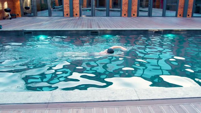 Outdoor pool scene with woman swimming freestyle crawl at twilight. Fitness clip focuses on coordinated stroke cycle, splashing water, and healthy recreational exercise