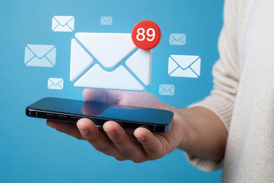 Close up of hand holding smartphone with digital email notification. Large white envelope icon floats above mobile device with red badge showing eighty nine unread messages. Person receives many new