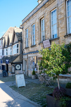 Burford, UK - April 7, 2026. Historic High Street Shops and Stone Facades in Burford Cotswolds. A high-detail vertical photograph showcasing traditional Cotswold stone boutique shops and storefronts a