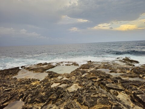 Karst limestone shore with tide pools and surf, wide view, Marsaskala