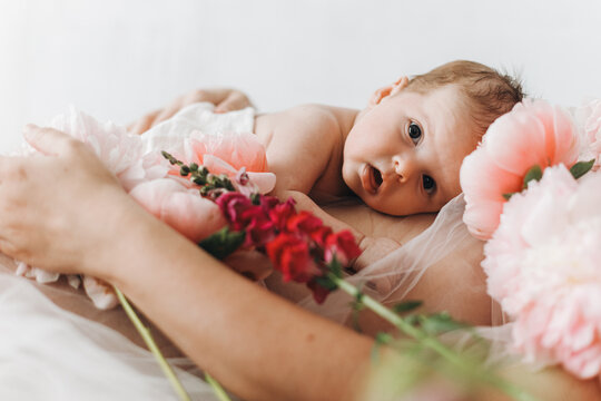 Happy Mothers day. Cute newborn baby lying on mother belly with peony flowers. Love and care concept. Portrait of baby son on mom tummy, tender moment. Adoption and maternity.