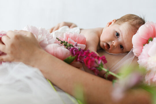 Cute newborn baby lying on mother belly with peony flowers. Love and care concept. Portrait of baby son on mom tummy, tender moment. Adoption and maternity. Happy Mothers day.