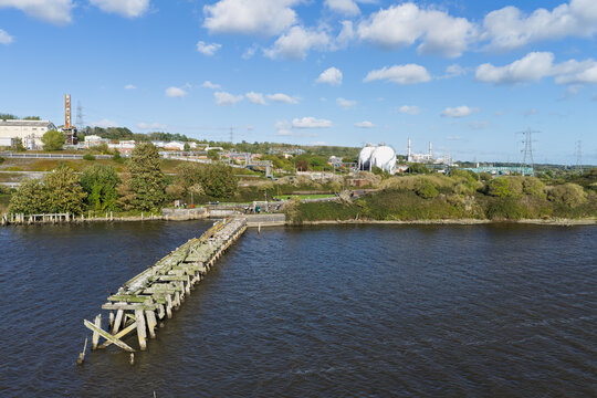 Aerial view of a chemical plant with large storage tanks and an old wooden pier extending into the river in the United Kingdom.