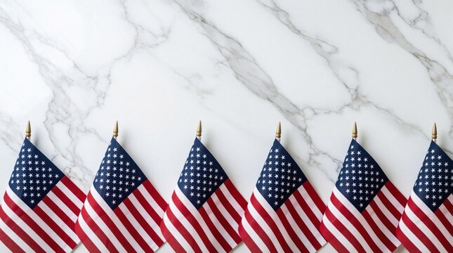 Six small American flags stand in row on white marble background. Patriotic US flags with red white, blue stars stripes arranged on elegant stone surface. Minimalist composition for July 4th