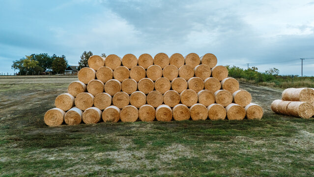 Aerial view of a large stack of round hay bales arranged in a pyramid shape in a harvested field under a cloudy sky in Utrine, Vojvodina, Serbia.