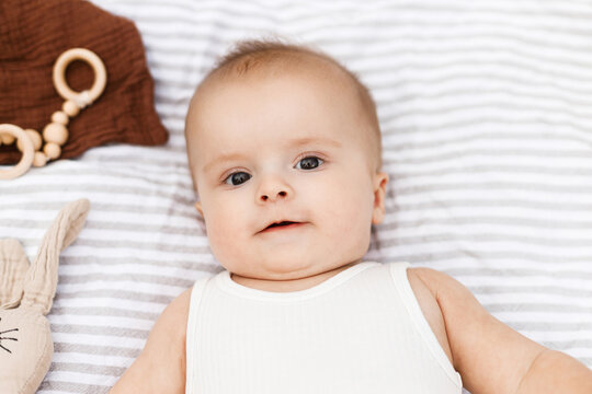 Beautiful happy baby lying on blanket with toys and teether in summer garden. Top view. Portrait of cute joyful baby relaxing in park, enjoying summer outdoors. Childhood