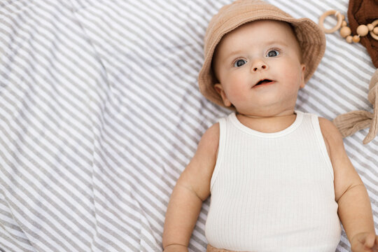 Beautiful happy baby lying on blanket with toys and teether in summer garden. Top view. Portrait of cute joyful baby relaxing in park, enjoying summer outdoors. Childhood