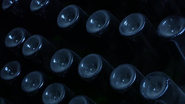 Dusty wine bottles aging in a dark cellar. Numerous dusty wine bottles resting on wooden racks in a dark, traditional cellar, slowly aging during the fermentation process of making sparkling wine