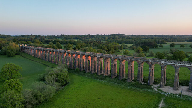 Aerial view of Ouse Valley Viaduct with its iconic brick arches stretching across the lush green countryside during the golden hour in Haywards Heath, England, United Kingdom.