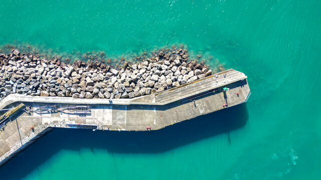 Aerial view of Torquay Harbour showing the concrete pier and protective rock breakwater extending into the turquoise sea in Torquay, England, United Kingdom.