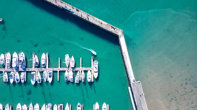 Aerial view of Torquay Harbour with numerous yachts and boats moored at the marina, a long stone pier extending into the turquoise sea, and calm water. Torquay, England, United Kingdom.