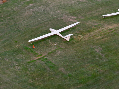 Aerial view of a white glider parked on a green grass airfield with a small orange traffic cone nearby United Kingdom.