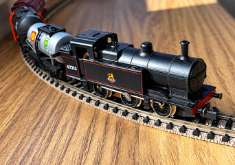 Detailed miniature steam locomotive curves across a model railway track in warm sunlight © brightimage