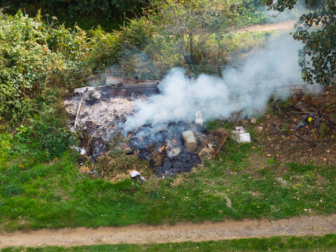 Aerial view of a small fire burning garden waste and debris with rising smoke in a rural field in the United Kingdom.