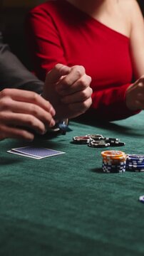 Players handle playing cards and arrange colorful poker chips on green felt during a close up casino card game at a poker table