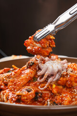 Metal tongs lifting spicy stir fried octopus over full serving plate © Donghyun Kim