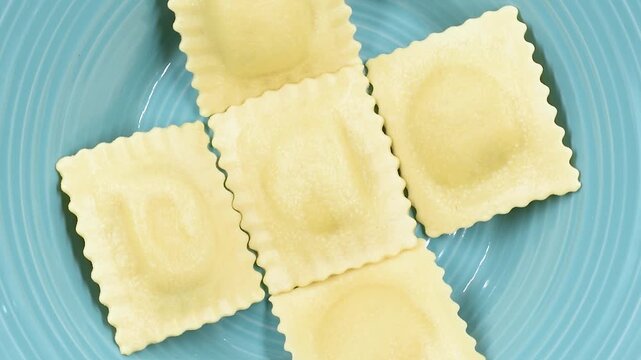 fresh Ravioli stuffed with ricotta cheese and asparagus, uncooked Italian egg pasta, close-up on a blue plate, rotating video.