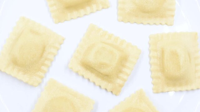fresh Ravioli stuffed with ricotta cheese and asparagus, uncooked Italian egg pasta, close-up on a white plate, rotating video.