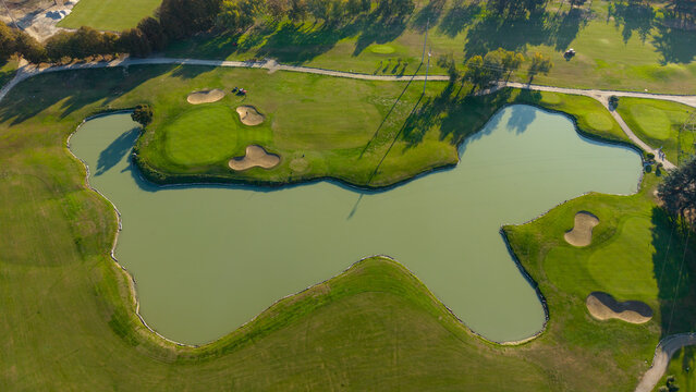 Aerial view of a golf course featuring a large water hazard, sand bunkers, and manicured green fairways in Milan, Lombardy, Italy.