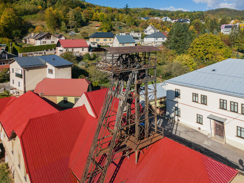 Aerial view of the historic Jama Ferdinand headframe surrounded by residential houses with red metal roofs and autumn trees in Ziar nad Hronom, Banskobystricky kraj, Slovakia.