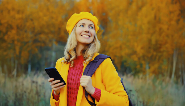 Stylish happy young woman with phone standing in autumn park