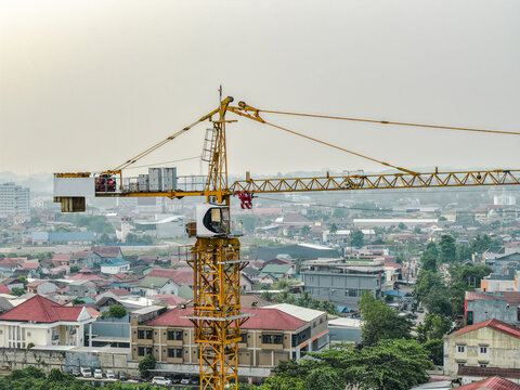 Aerial view of a yellow tower crane standing over a dense urban landscape with residential rooftops and buildings in Samarinda, East Kalimantan, Indonesia.