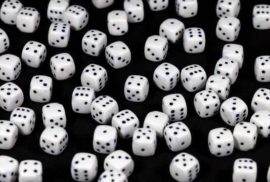 Close-up of numerous white gaming dice on black surface. Many white dice on dark background. Scattered white dice on a black background