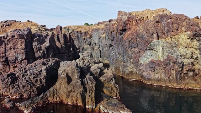 Rock formations rise around a tidal pool along a coast, with sunlight on the cliff faces and a clear sky overhead during the day.