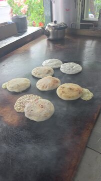 High-angle close-up shot of authentic handmade Salvadoran pupusas filled with cheese and beans cooking on a large metal griddle plate with steam rising. Features melted cheese crisped on the hot surfa