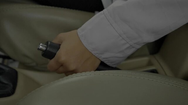 Cinematic close-up footage of driver hand pulling parking handbrake lever inside car.