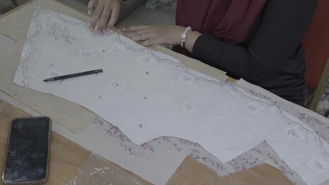 Cinematic footage of a woman fashion designer tracing traditional batik pattern on fabric in a workshop. Close up of hands drawing sewing pattern template for textile craft.