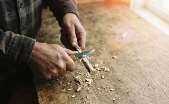 Middle-aged man whittling wood with a pocket knife in a workshop, craft hobby concept