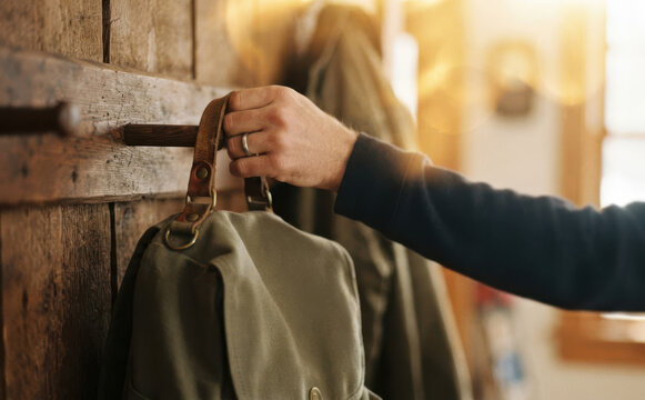 Close up of man hand hanging canvas backpack on wooden coat rack in hallway at home