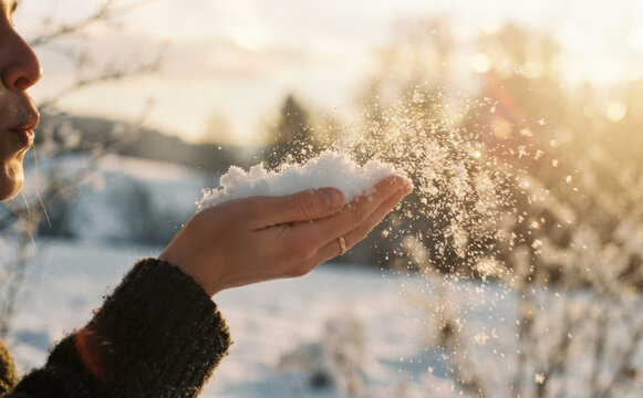 Young woman blowing snow from her hands outdoors in winter landscape during golden hour sunlight scenic view
