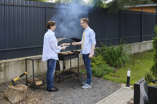 Wife assist her husband to grill meat skewers in a backyard/ They enjoying a sunny afternoon. Laughter and conversation fill the air as they prepare for a relaxing meal