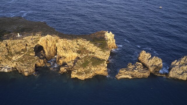 Drone shot, rocky coastline of an island at dusk with cave and clear water, morning light, islet of Tsichli Babas, island of Sfaktiria, Navarino Bay, Pylos, Peloponnese, Greece