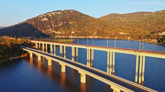 Two road bridges span a reservoir near wooded hills, with the surrounding landscape lit by the low sun in the late afternoon.