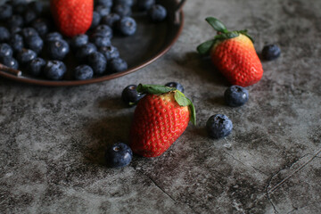 Fresh Strawberries and Blueberries on scattered across textured surface, showcasing nature vibrant bounty. Organic Healthy food. © Warunporn
