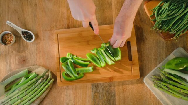 Vegetables top view, hands preparing fresh green asparagus, green beans, broccoli and bell pepper on wooden cutting board, healthy cooking flat lay