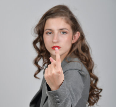 Junge Frau im grauen Blazer zeigt demonstrativ den Mittelfinger in die Kamera. Provokation, Ablehnung, Wut, Frust, Beleidigung, Protest, Respektlosigkeit und starke nonverbale Kommunikation.