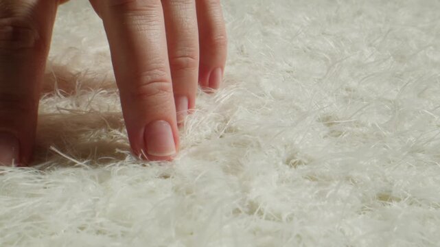 White fur texture with hand touching, close up of fluffy faux fur and natural sheepskin rug, soft long hair fur background in fur shop from Turkish fur factory production